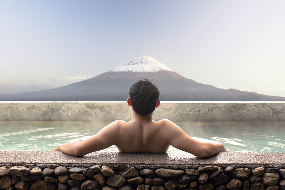 Asian man relaxing in outdoor Japanese bath with Mt. Fuji view