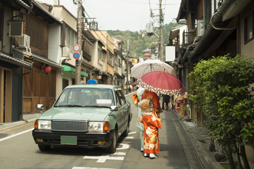 Vintage street scene in Kyoto province, Japan with taxi car and females wearing Yukata and handling traditional umbrellas